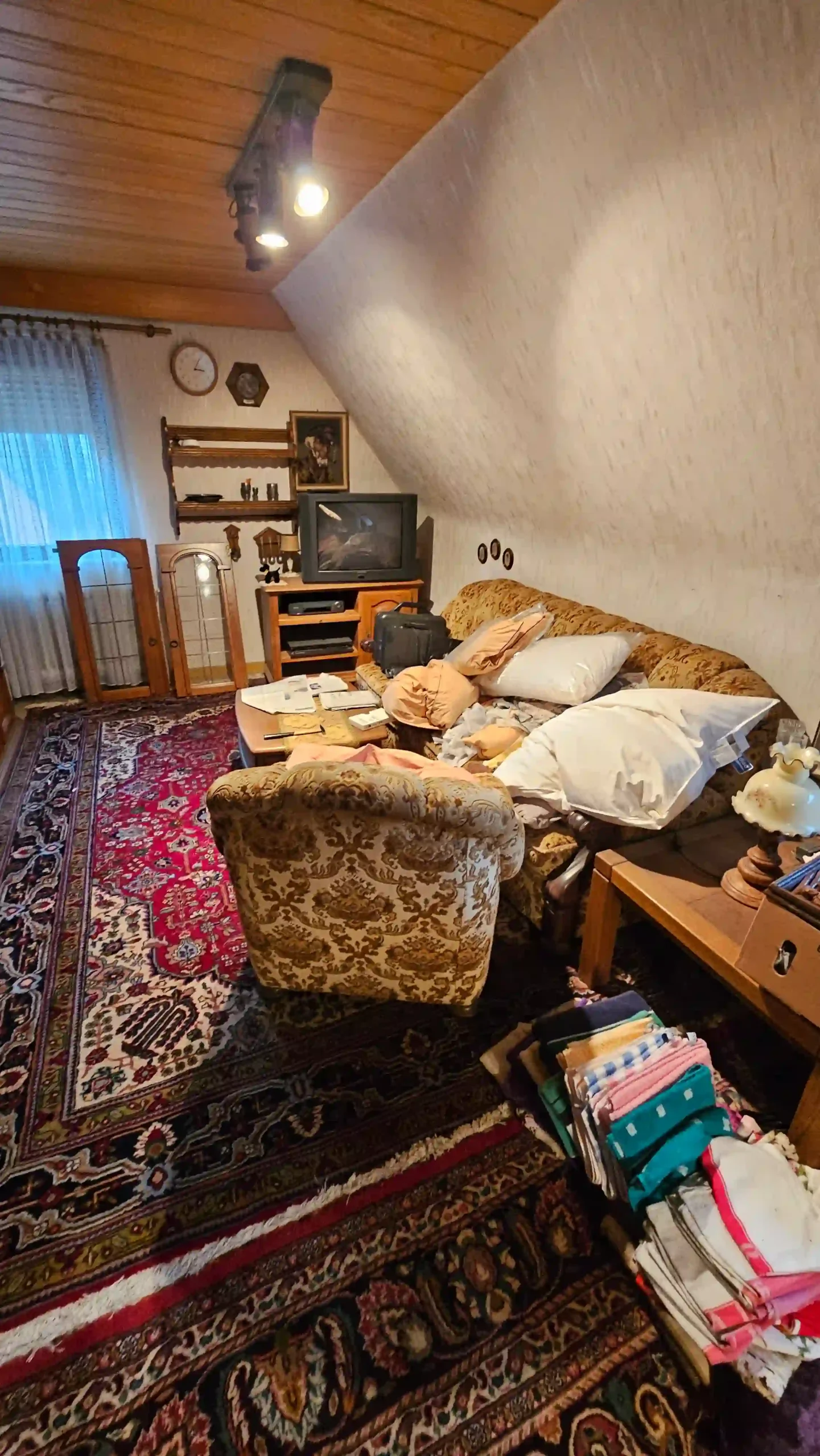 Haushaltsauflösung Wohnzimmer unter einer Holzdecke mit Sofa, Sessel, Fernseher und abgelegtem Hausrat