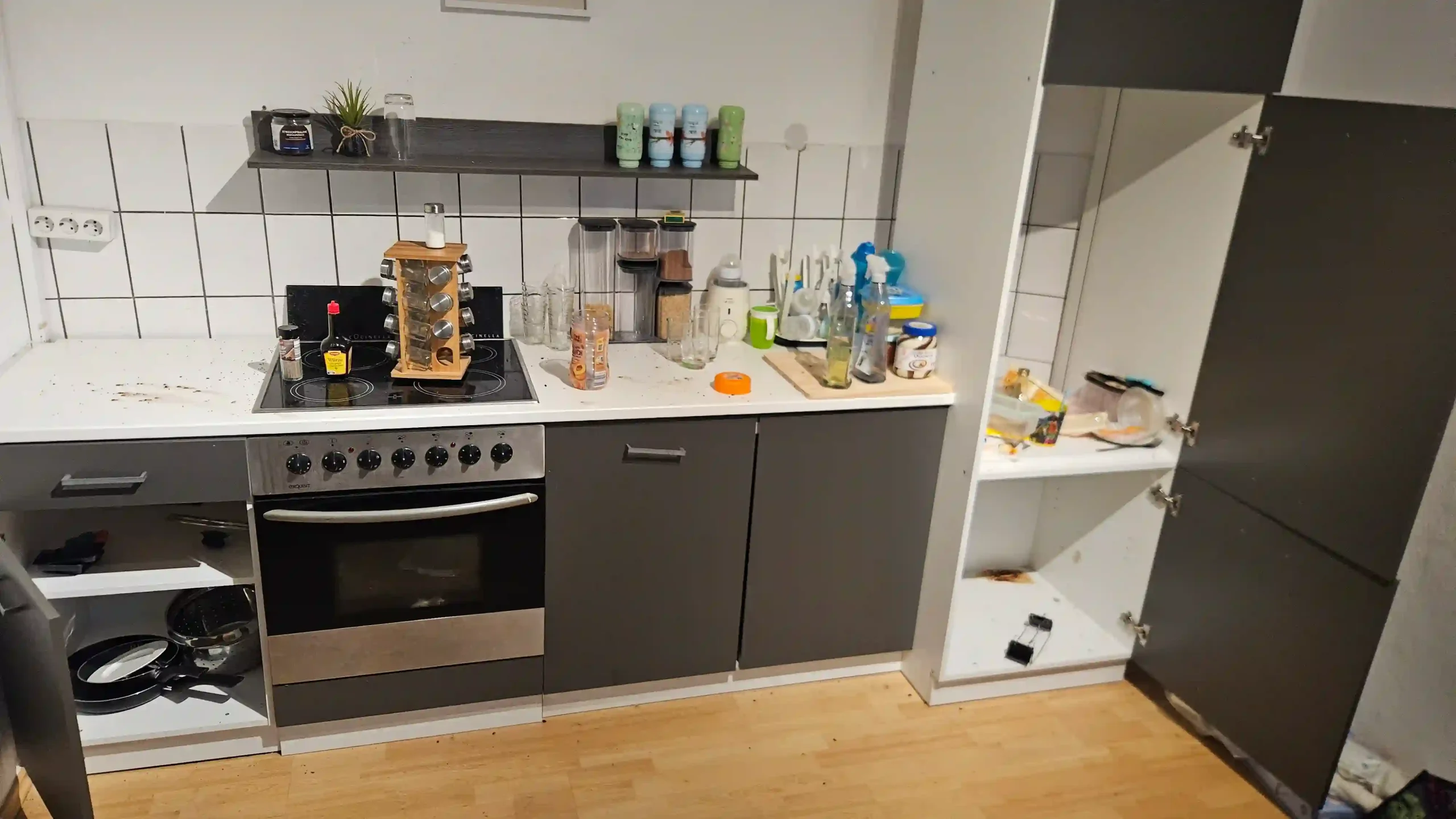 Haushaltsauflösung Graue Einbauküche mit offenen Schränken, Backofen, Geschirr und Vorräten auf der Arbeitsplatte
