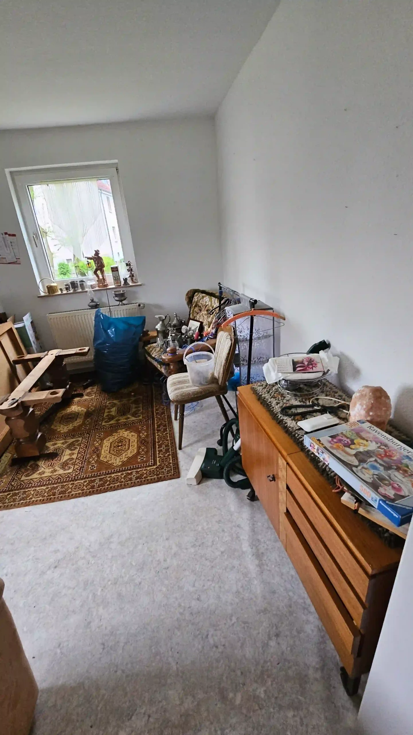 Haushaltsauflösung Wohnraum mit Holzkommode, Stühlen, Tischteilen, Teppich und zusammengestelltem Hausrat